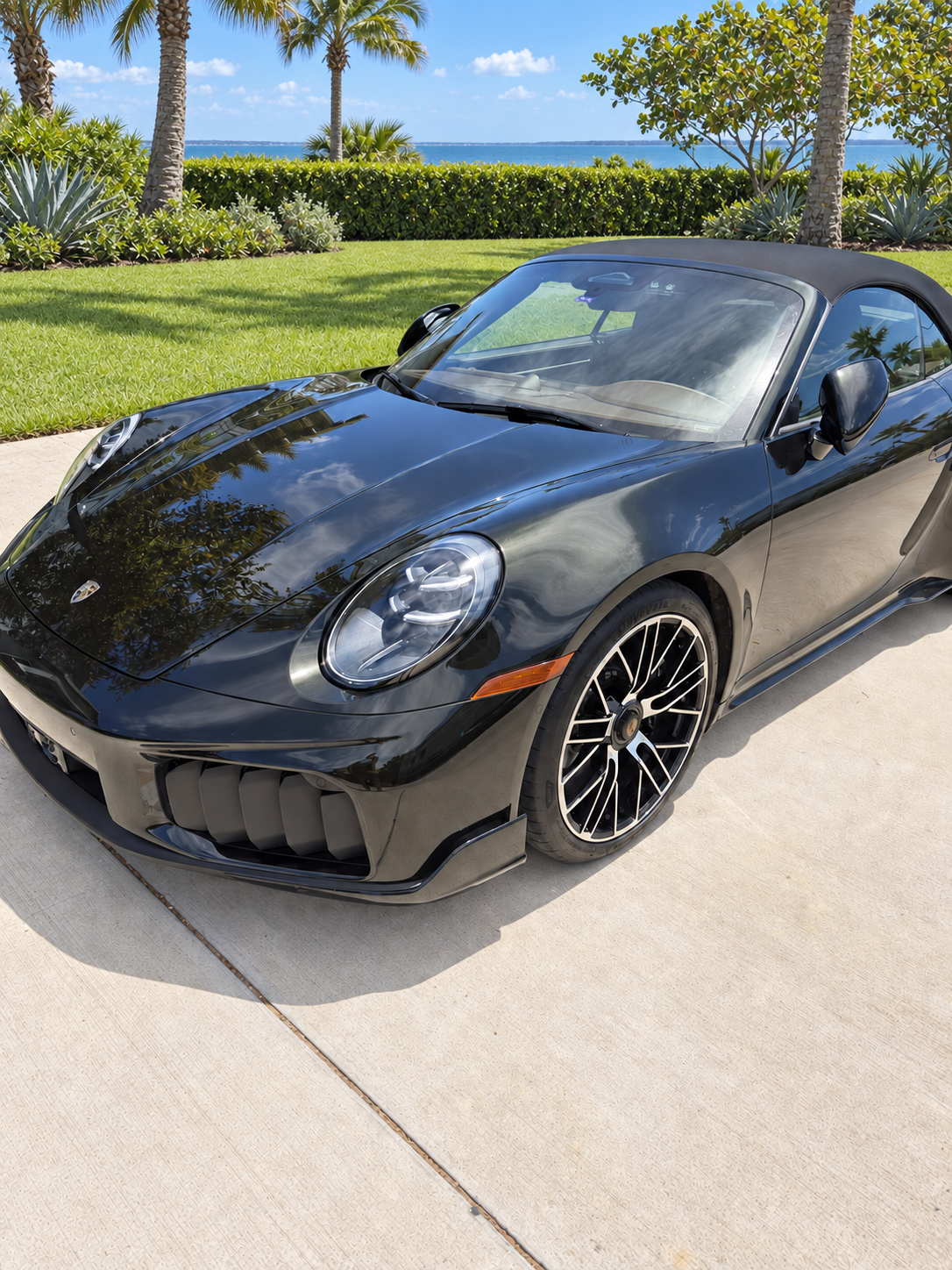 Front three-quarter view of the Dark Olive Green Porsche 911 Turbo S Cabriolet against manicured coastal landscaping